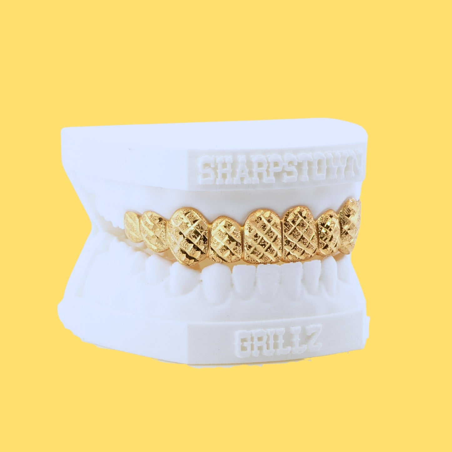 Custom yellow gold top grillz with diamond cut crosshatch pattern and diamond dust texture on a white dental cast.