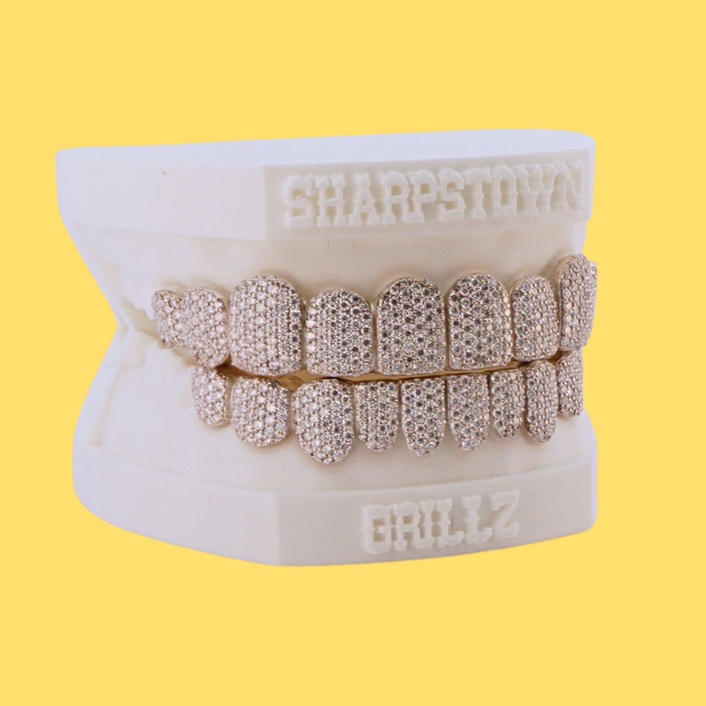 Custom top and bottom full set iced-out diamond grillz on a white dental cast with yellow background.