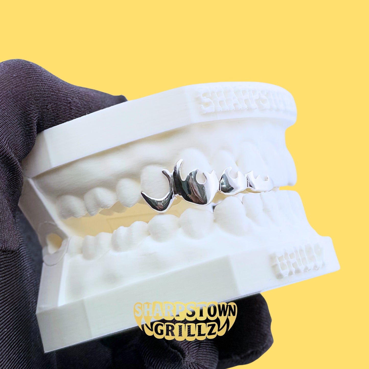 Front view of custom silver open face flame teeth caps held in a gloved hand