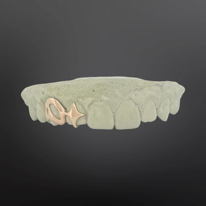 Teeth-shaped grill with gold fish charm on a dark background