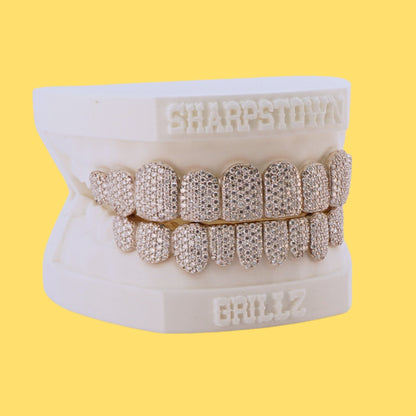 Custom top and bottom full set iced-out diamond grillz on a white dental cast with yellow background.
