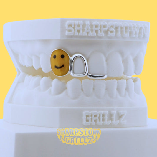 Front view of custom silver tooth grill featuring a yellow enamel smiley face icon and open window frame.