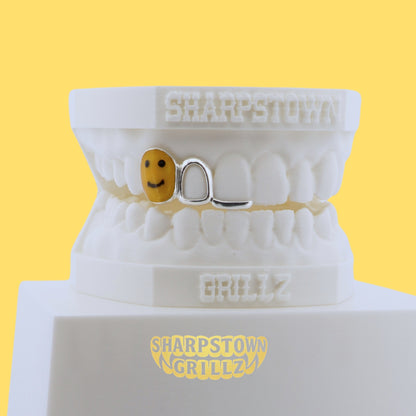 Silver open face tooth grill with custom yellow smiley face enamel inlay fill on a yellow background.
